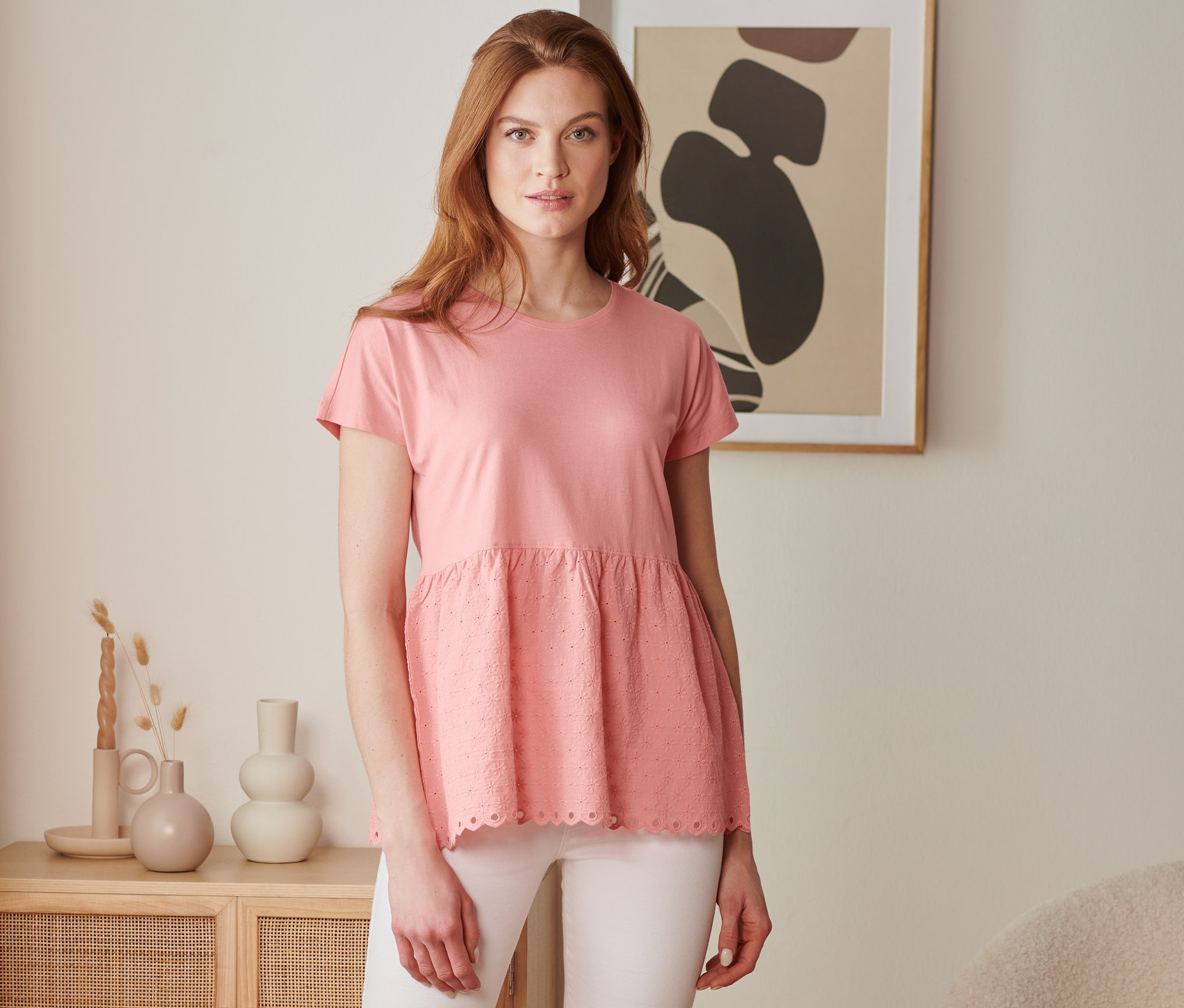 Une femme porte un t-shirt bimatière à broderie corail et un pantalon blanc.