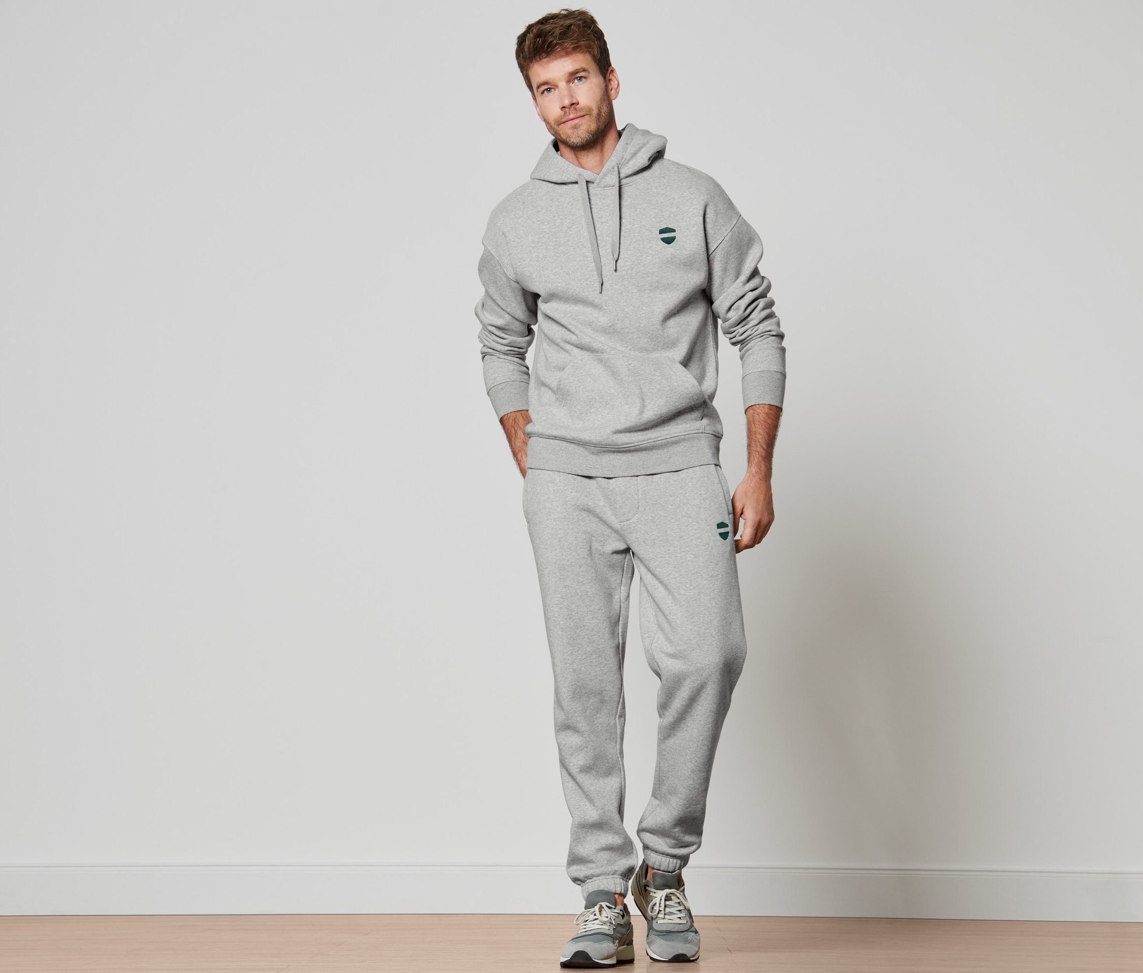 Un homme debout portant un sweat à capuche gris chiné et un pantalon de jogging.