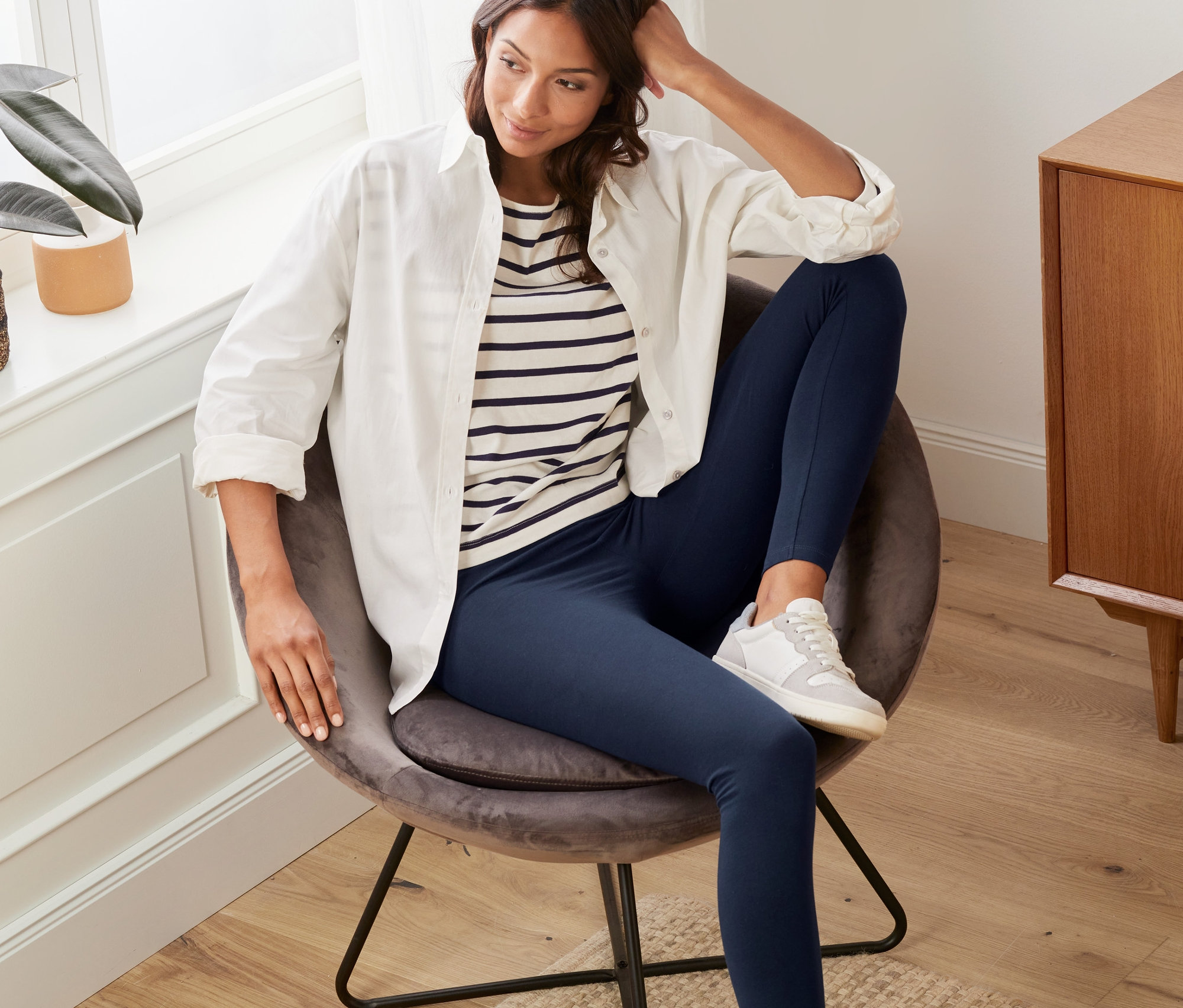 Femme assise dans un fauteuil portant un legging bleu foncé.