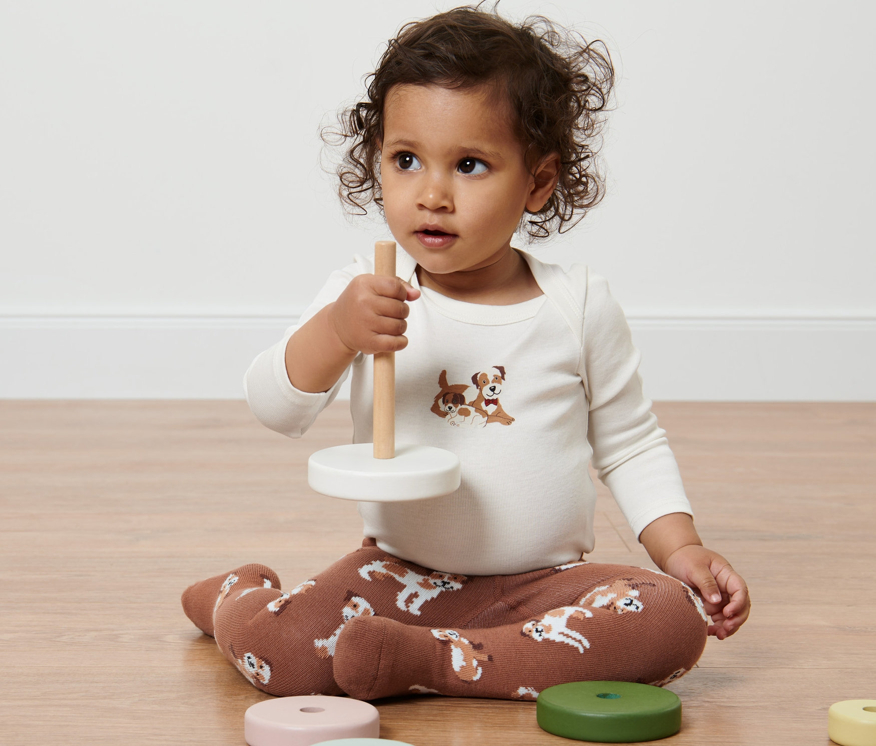 Un enfant est assis par terre et joue avec un jouet. Il porte 2 collants pour bébés avec un motif de chien.