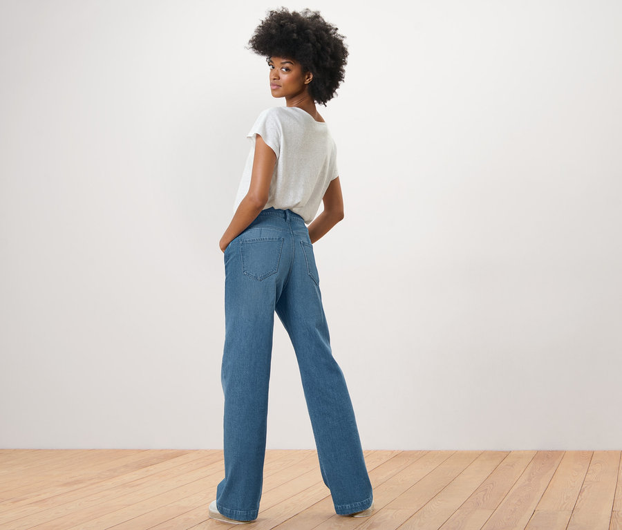 Une femme regarde par-dessus son épaule et pose en jean palazzo – coupe « Neni » et un t-shirt blanc.