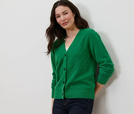 Une femme pose en cardigan vert avec structure tricotée et un jean bleu marine.