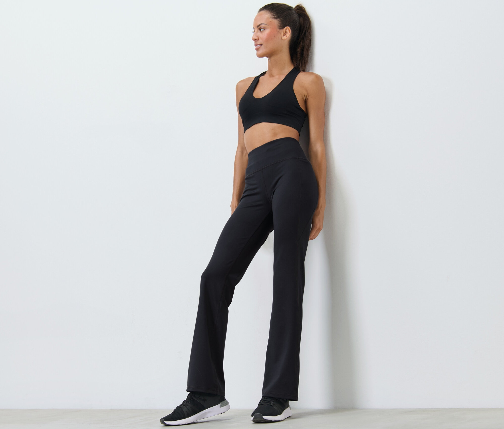 Une femme pose en soutien-gorge de sport noir et pantalon de sport modelant.