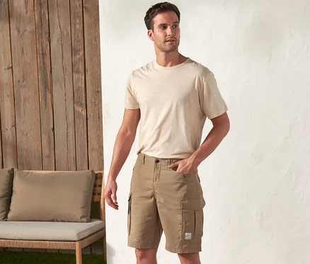 Un homme se tient à l'extérieur et porte un t-shirt beige et un short kaki « Work wear ».
