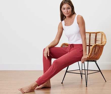 Femme assise sur une chaise en rotin portant un pantalon de pyjama et un débardeur blanc.