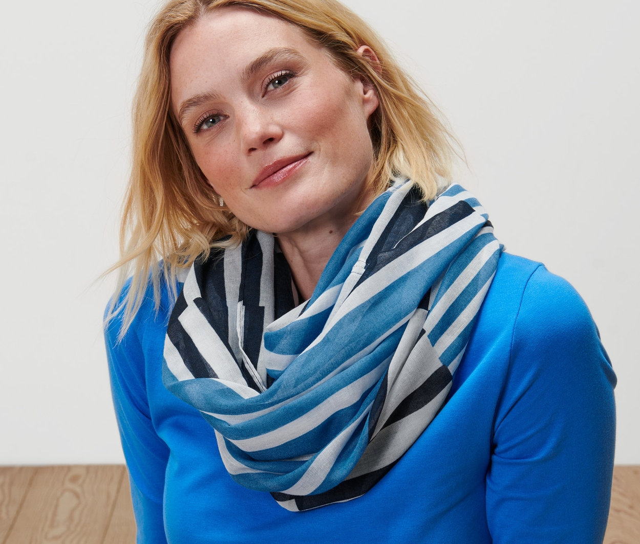 Femme blonde assise par terre portant un col écharpe à rayures.