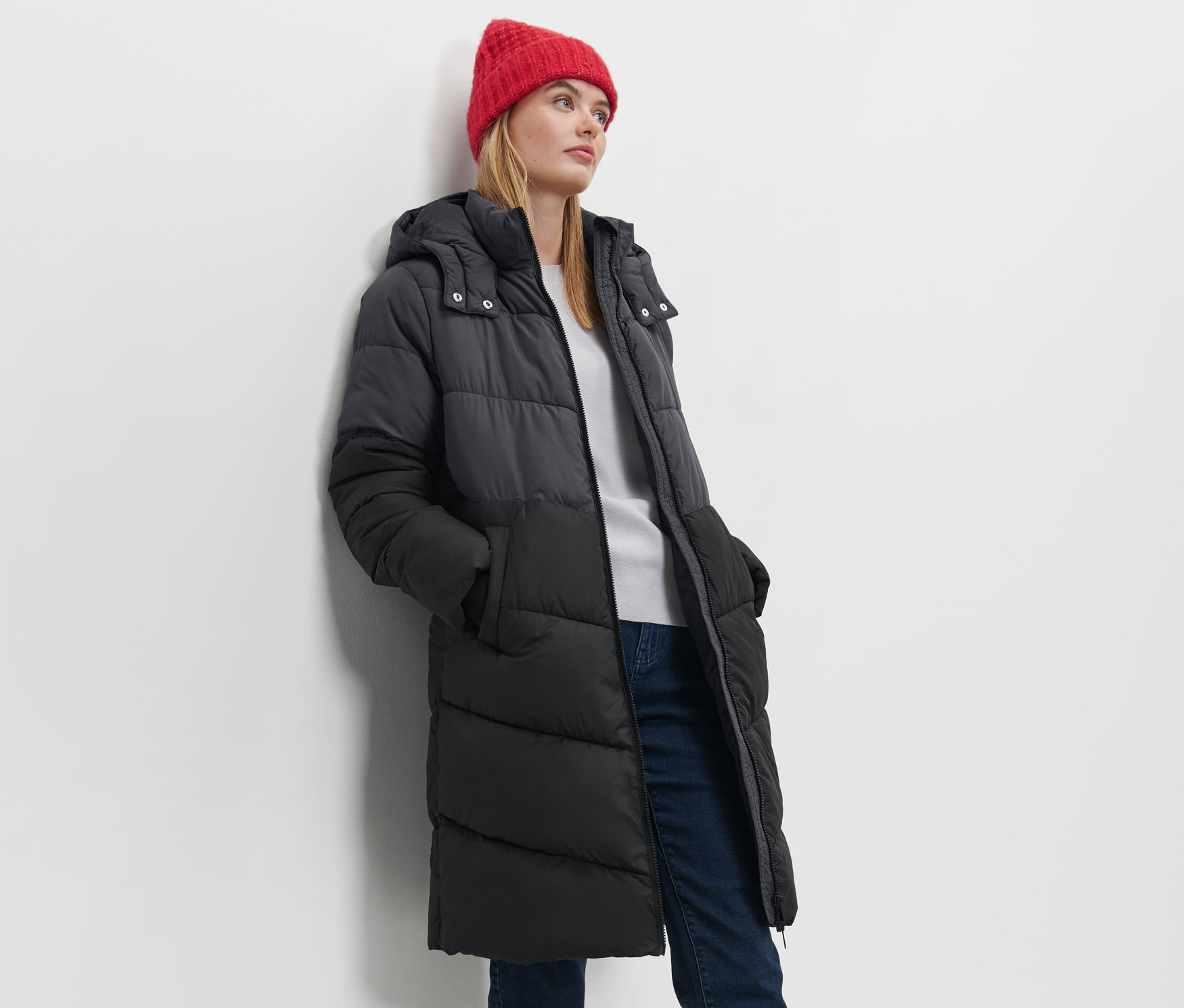 Femme posant en manteau matelassé à capuche et bonnet rouge.