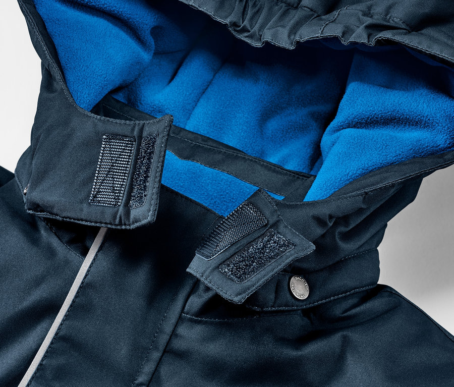 Gros plan sur une veste de ski pour enfant avec capuche et doublure polaire bleue.
