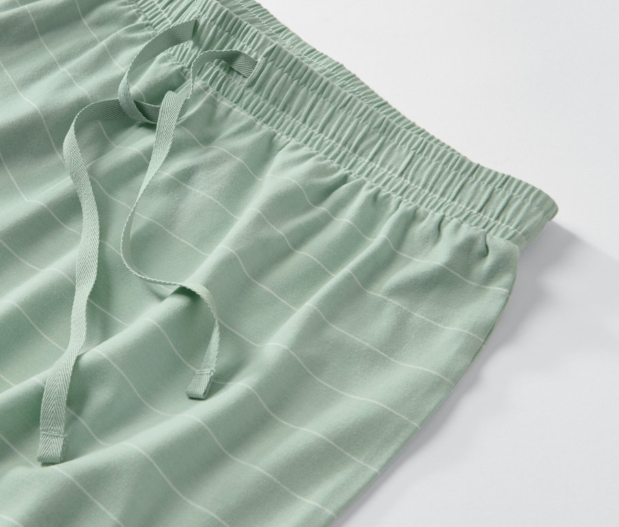 Détail d'un pantalon de pyjama vert avec des rayures blanches et un cordon de serrage.