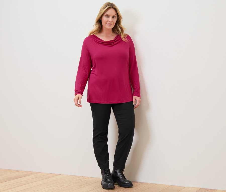 Une femme debout porte un chemisier à col cascade et un pantalon en bengaline.