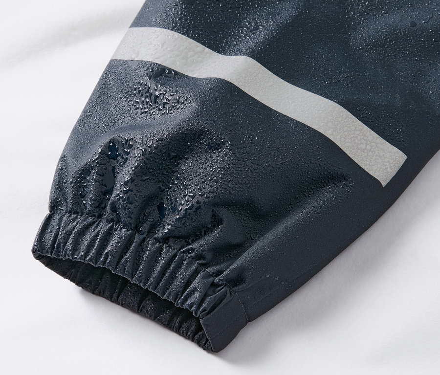 Gros plan sur la manche d'un pantalon de pluie pour enfant bleu foncé avec une bande réfléchissante et des gouttes d'eau.
