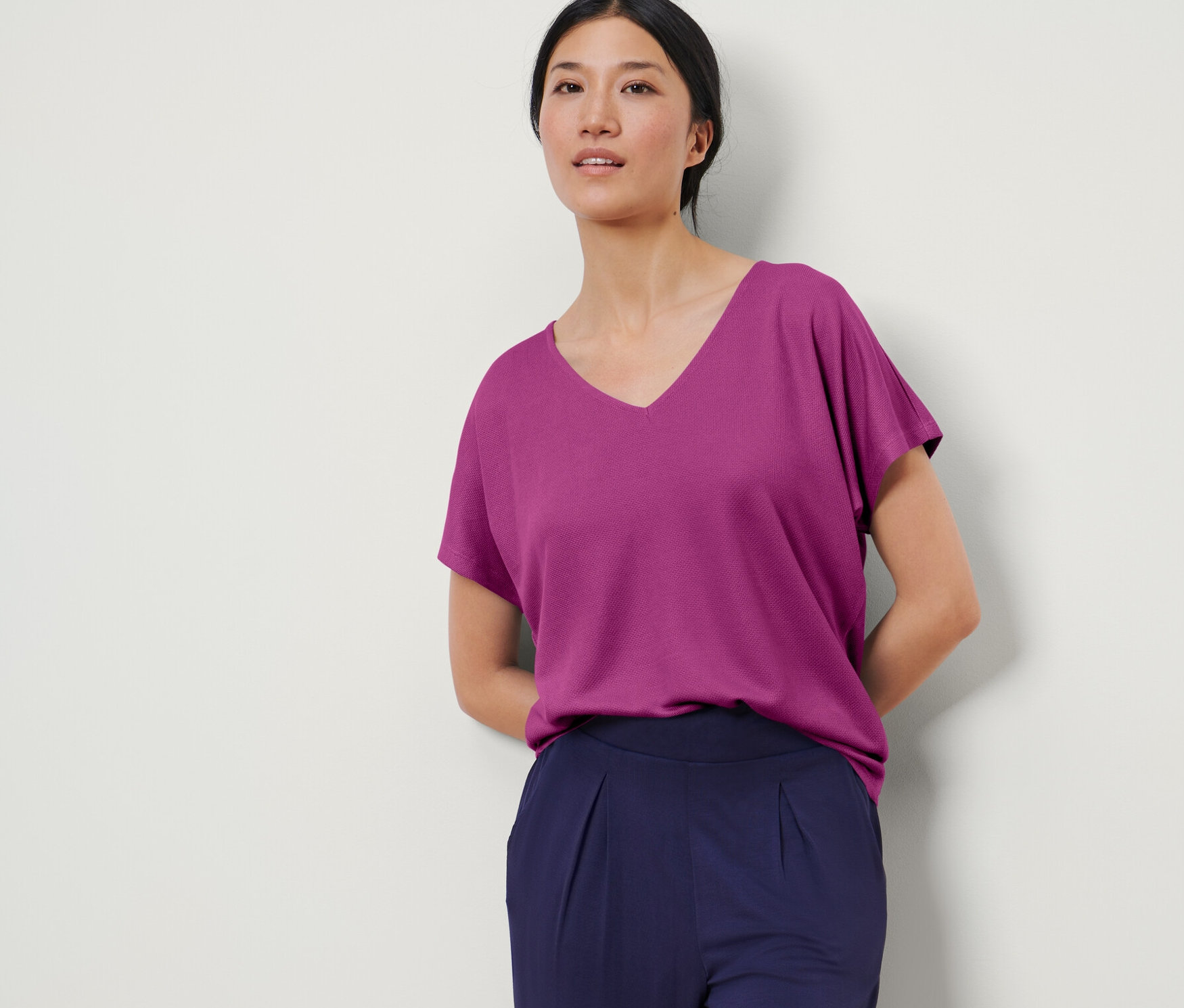 Une femme pose portant un chemisier structuré couleur baie et un pantalon bleu marine.