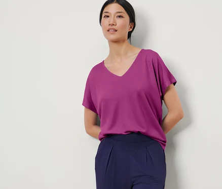 Une femme pose portant un chemisier structuré couleur baie et un pantalon bleu marine.