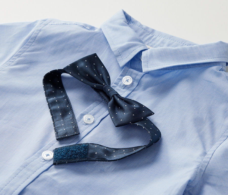 Chemise bleue pour enfant avec nœud papillon à pois blancs, le nœud papillon est ouvert.