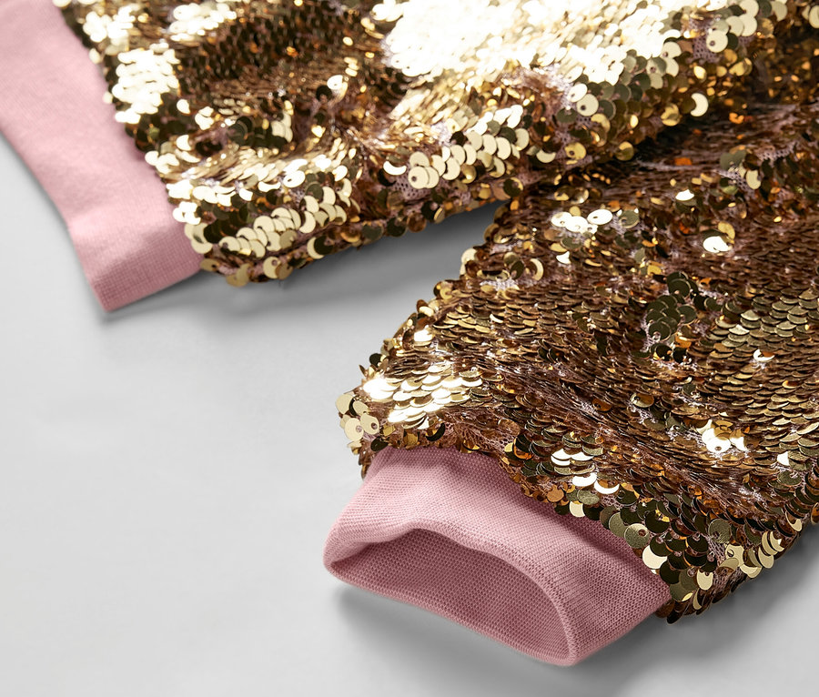 Détail d'une veste à paillettes pour enfants avec des poignets rose clair.