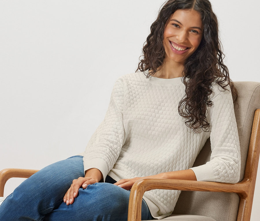 Une femme assise dans un fauteuil porte un pull-over en maille structurée.