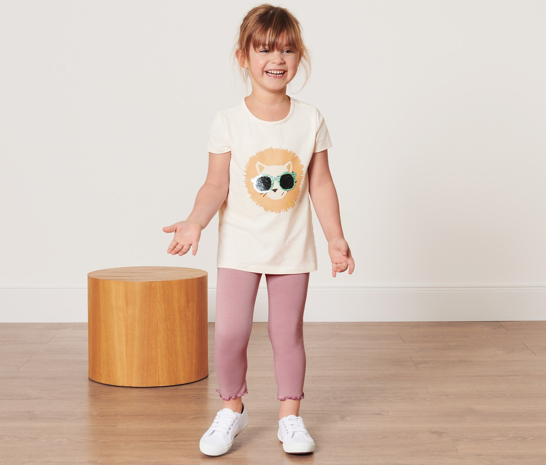 Une fillette souriante porte un legging pour enfant et un t-shirt avec un imprimé de lion.