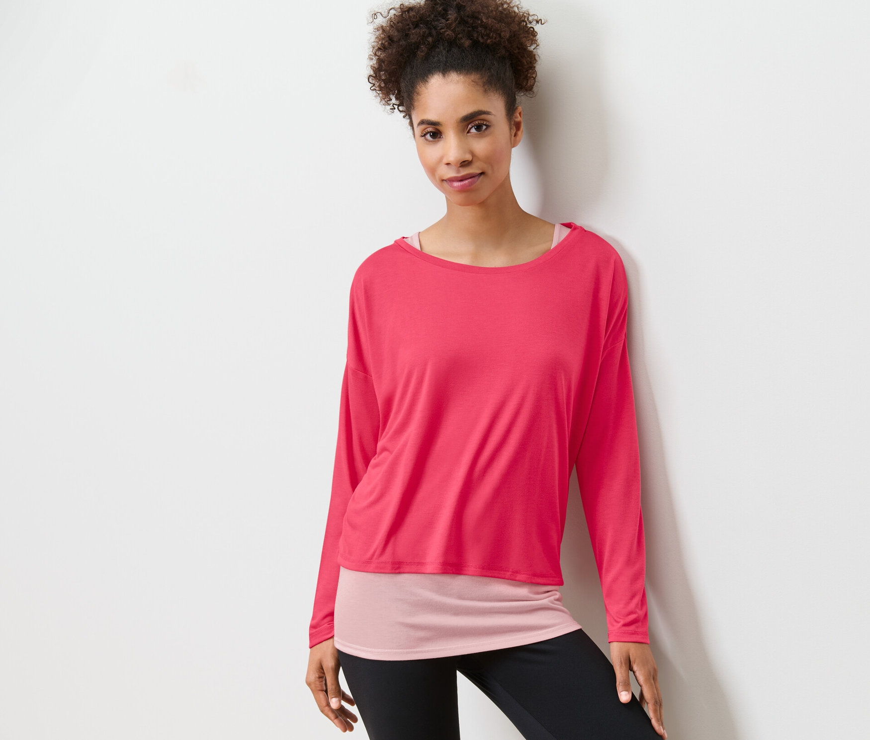 Femme posant dans un t-shirt de sport 2 en 1 rose vif et un legging noir.