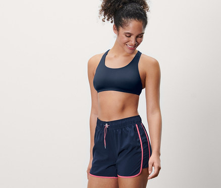 Femme souriante portant un short de bain et un soutien-gorge de sport.
