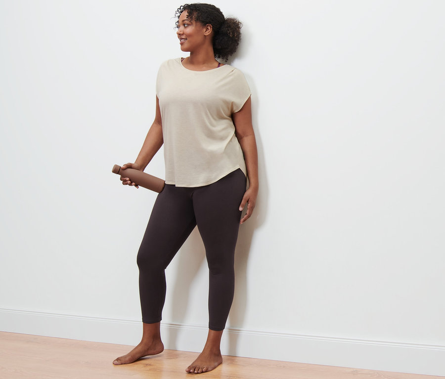Une femme tient une bouteille d'eau marron et porte un t-shirt de sport beige et un legging de sport.