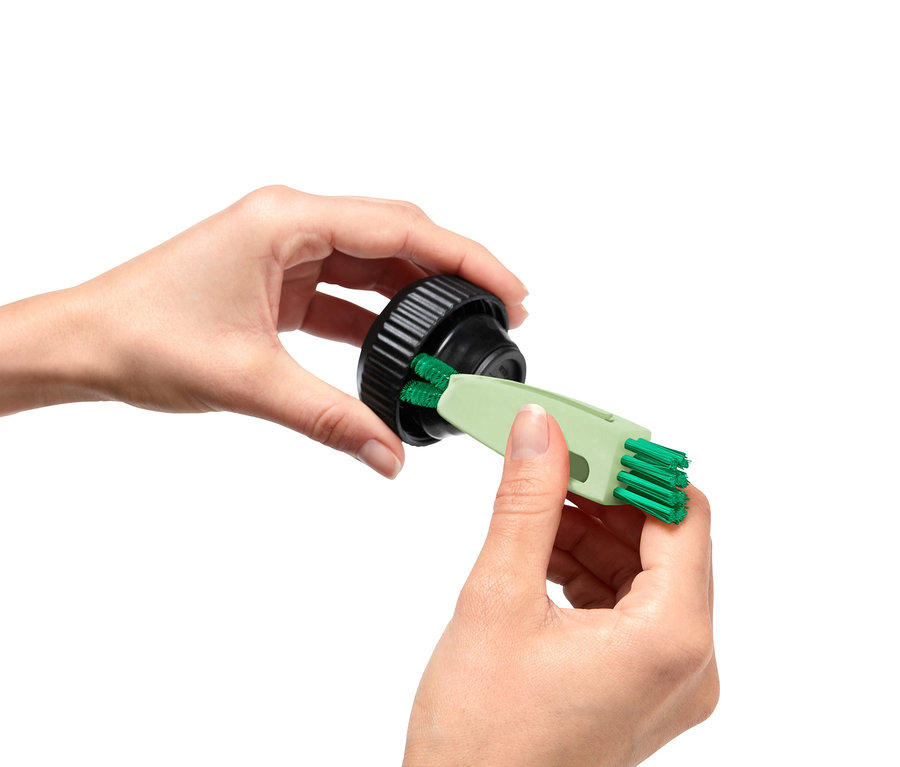 Une femme nettoie un bouchon noir avec une brosse multifonction 3 en 1 verte.