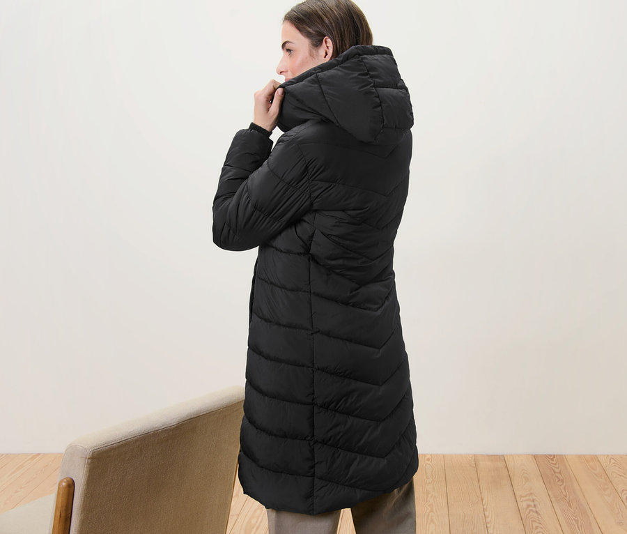 Une femme ajuste la capuche d'un manteau matelassé à capuche noir.