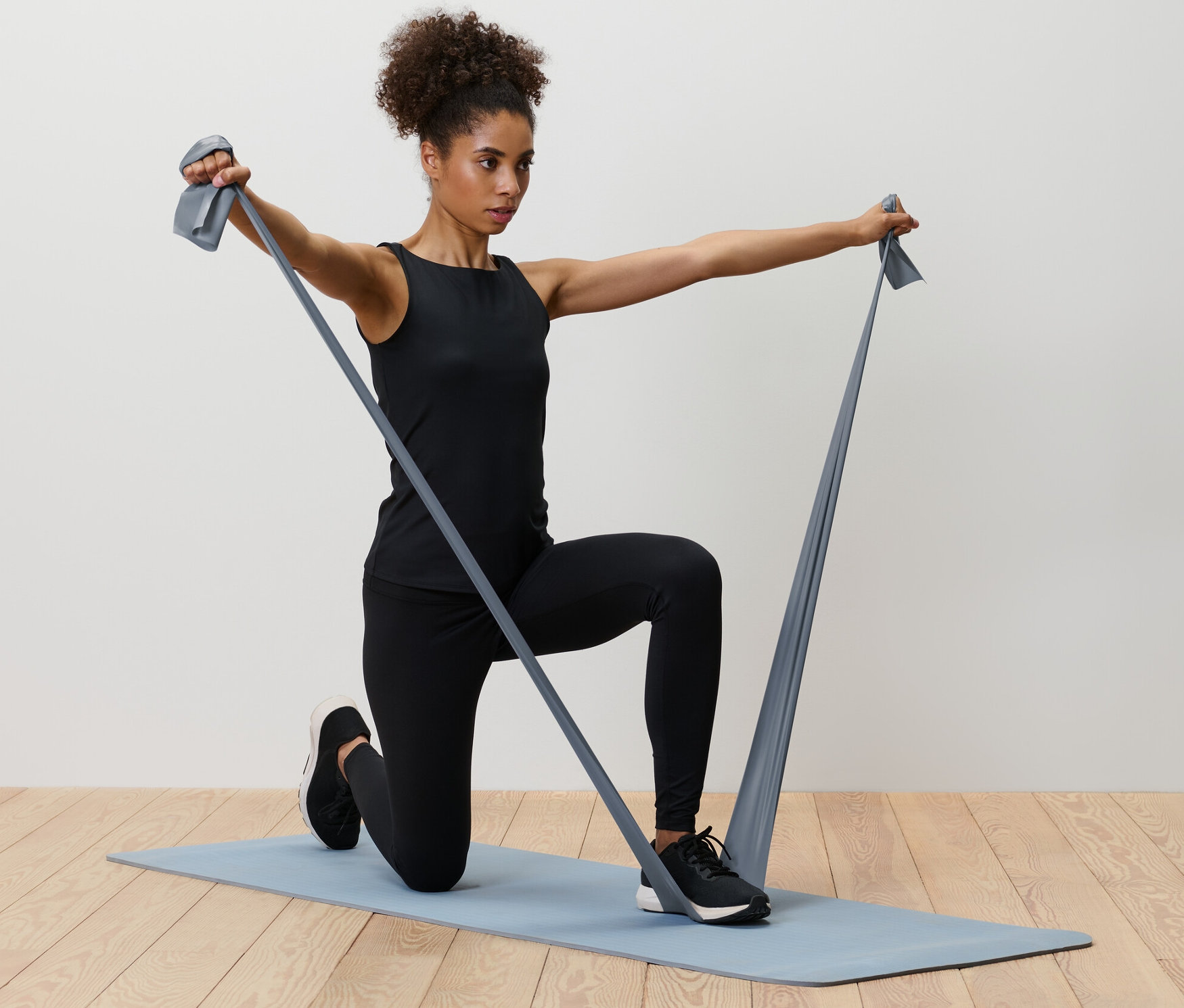 Femme agenouillée sur un tapis faisant des exercices avec 2 bandes de fitness.