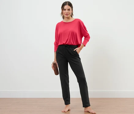 Une femme debout tenant une bouteille d'eau, portant un pantalon de survêtement noir.
