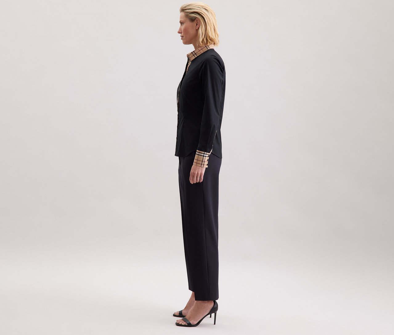 Femme de profil portant un chemisier en popeline à carreaux Seidensticker, un pantalon foncé et des sandales à talons.