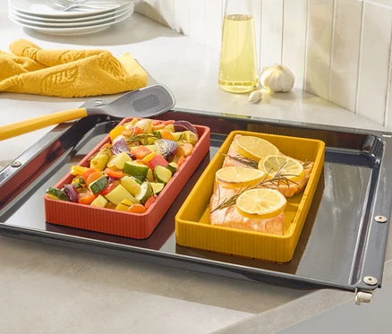 Sur une plaque de cuisson se trouvent deux plats à gratin colorés, un avec du saumon et du citron, l'autre avec des légumes.