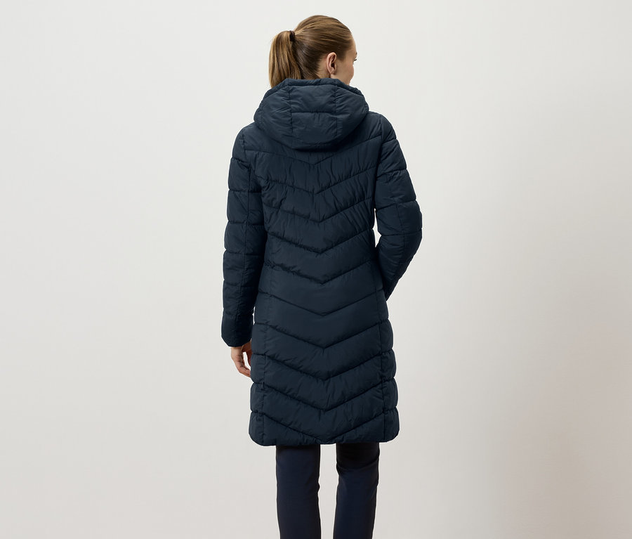 Vue arrière d'une femme aux cheveux bruns attachés en queue de cheval portant une longue veste matelassée bleu marine avec une capuche.