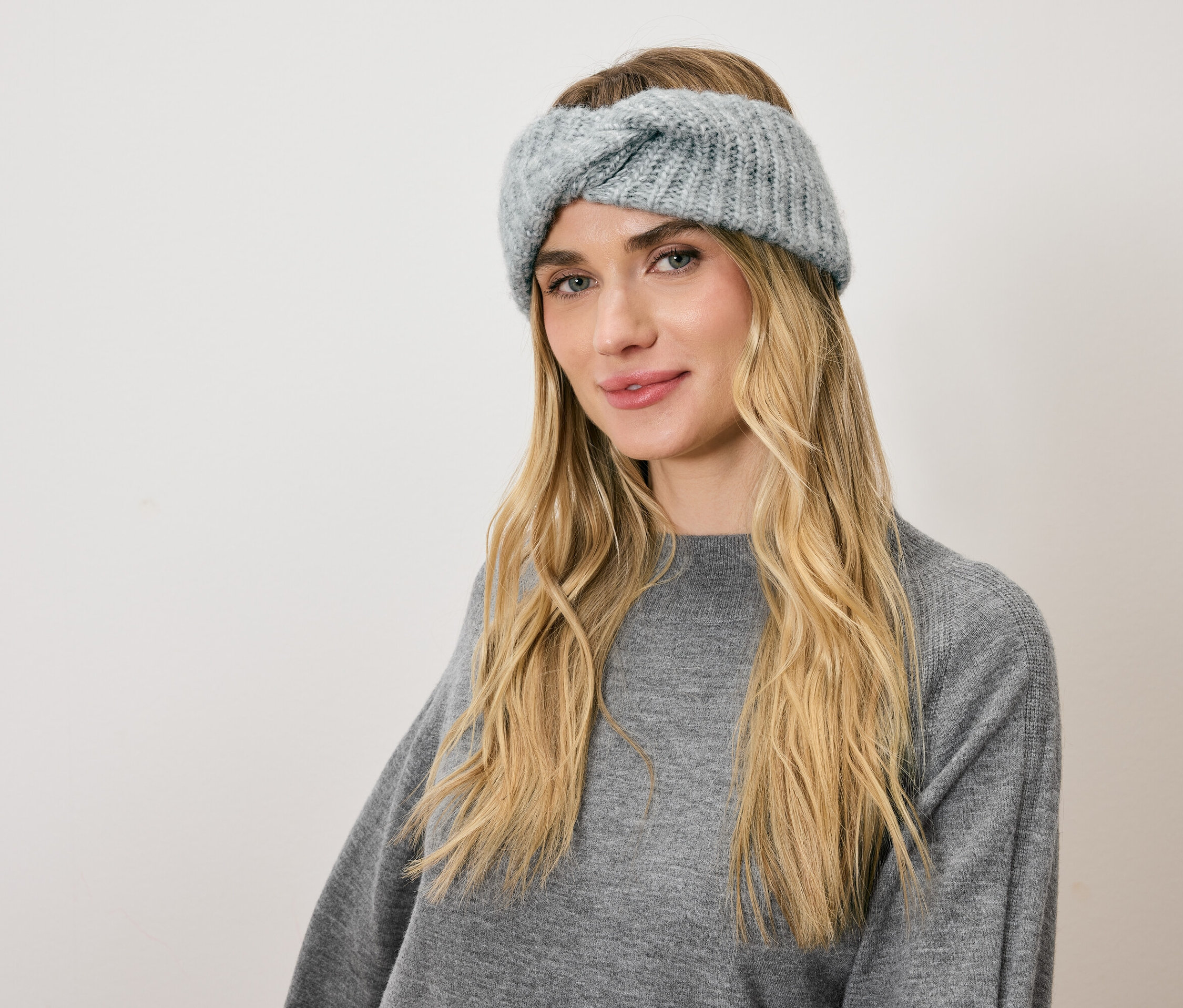 Portrait d'une femme blonde portant un turban tricoté bleu et un pull gris.