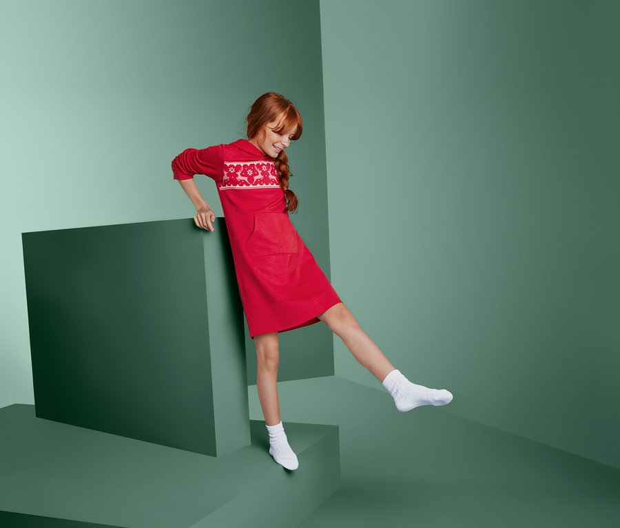 Fillette en robe d’intérieur rouge posant à côté d’un cube vert.