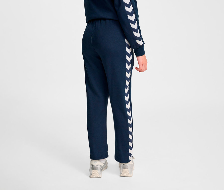 Personne vue de dos portant un pantalon en poly bleu marine HUMMEL HMLJR Archive Regular avec des chevrons blancs sur le côté.