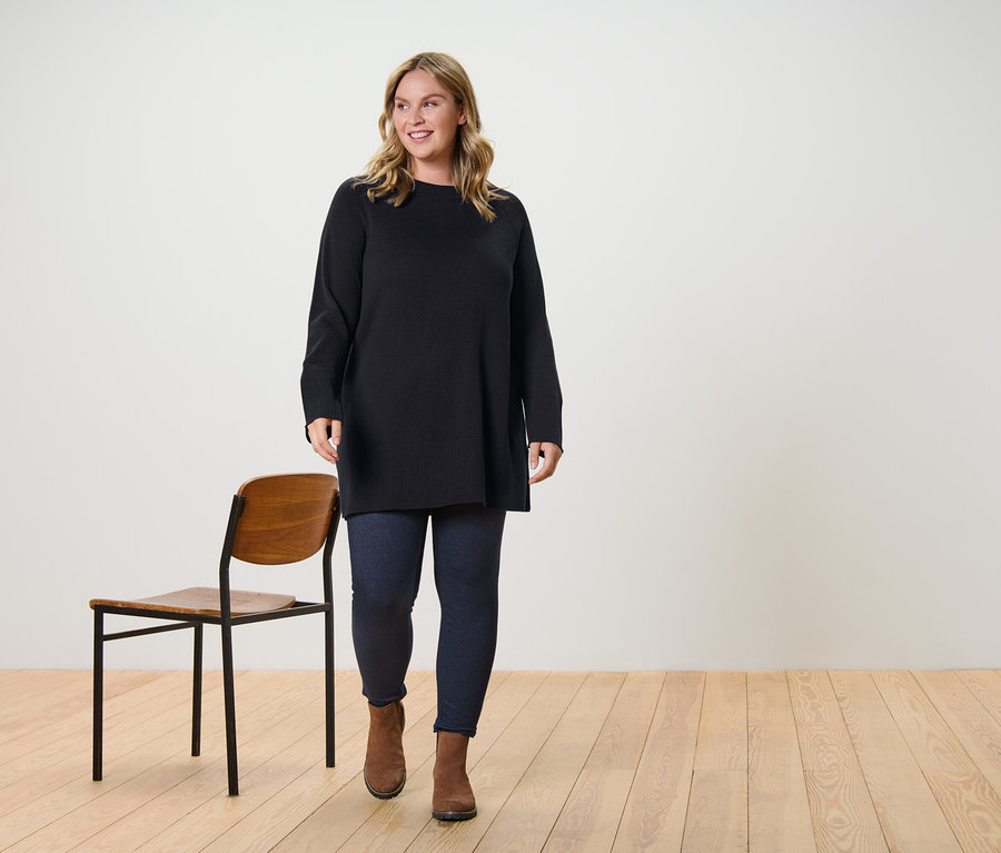 Une femme marche et porte un long pull en maille marron foncé et un legging doublé à l’aspect jean.