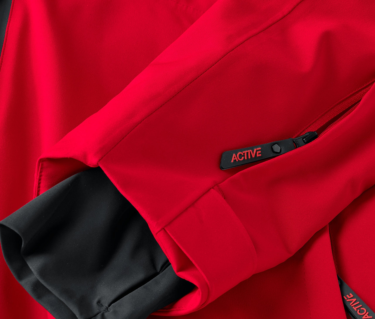 Détail d'une veste rouge avec des éléments noirs et une fermeture éclair avec l'inscription ACTIVE.