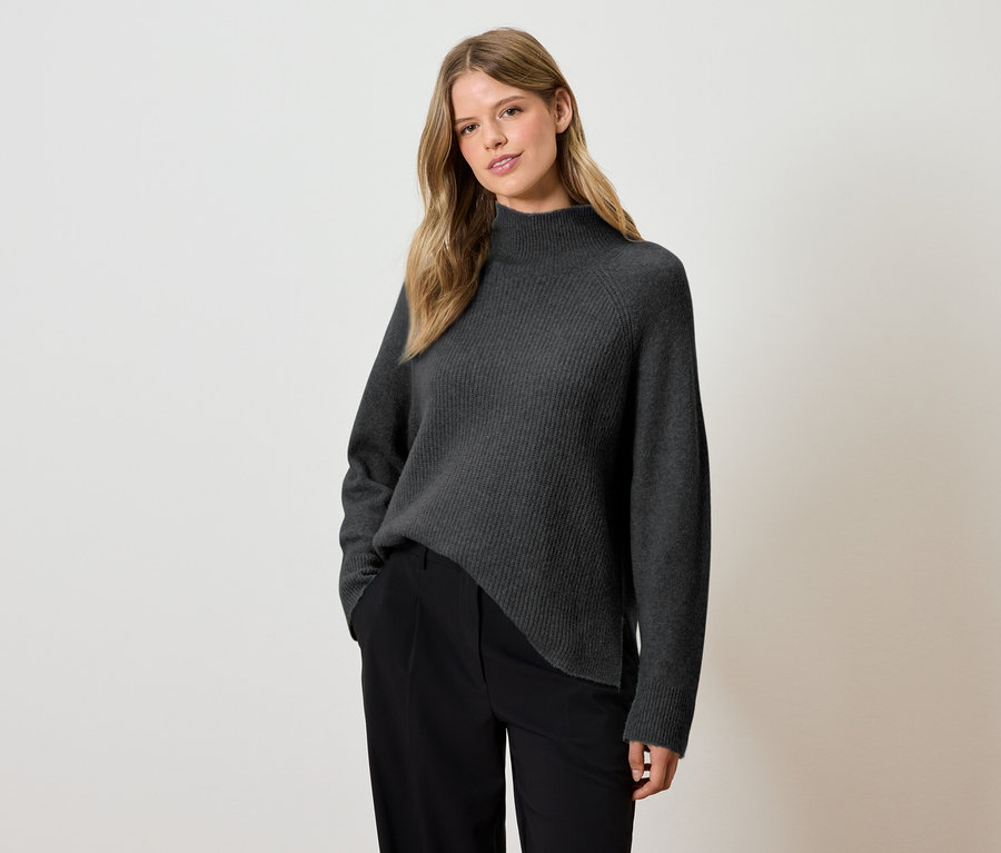 Femme posant dans un pull à col roulé gris et un pantalon noir.