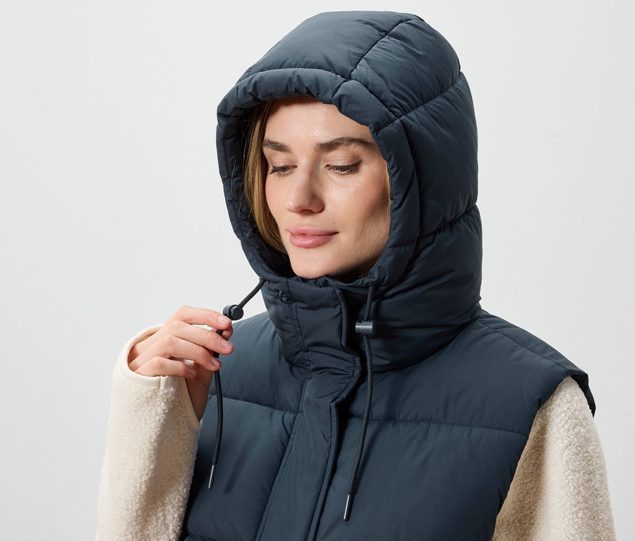 Une femme ajuste la capuche d'un gilet matelassé bleu foncé.