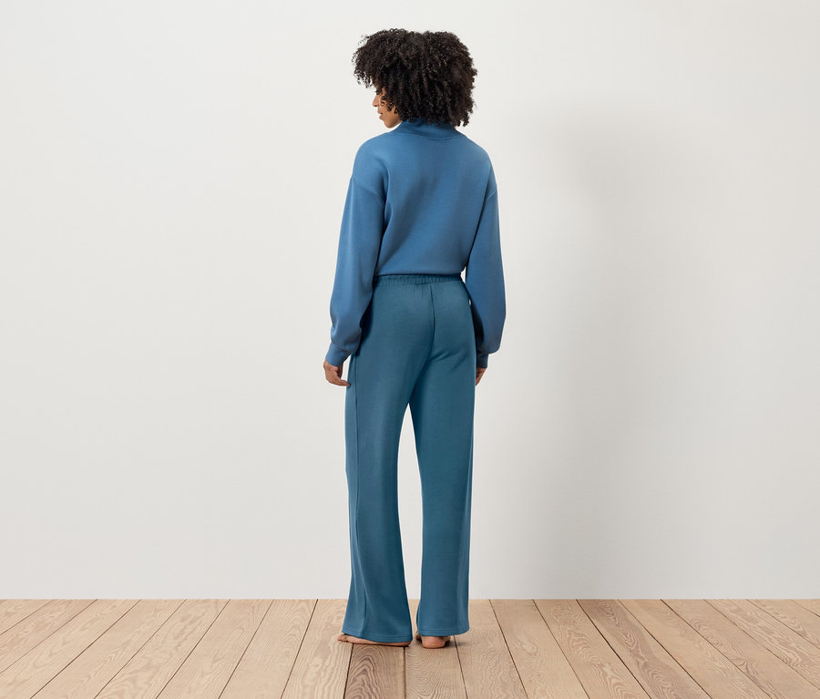Vue de dos d'une femme aux cheveux bouclés foncés, portant un sweat-shirt bleu et un pantalon large.