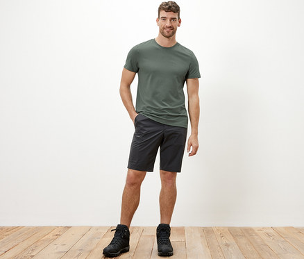 Un homme portant un t-shirt fonctionnel kaki, un short noir et des bottes noires.