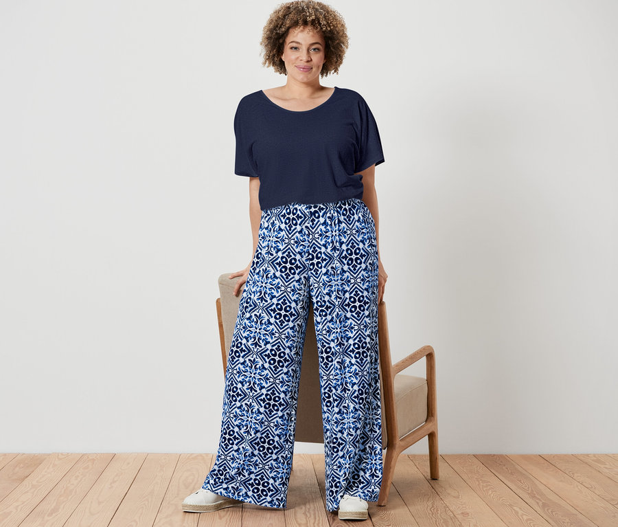 Une femme pose avec un t-shirt bleu marine en lin mélangé et un pantalon palazzo imprimé bleu.