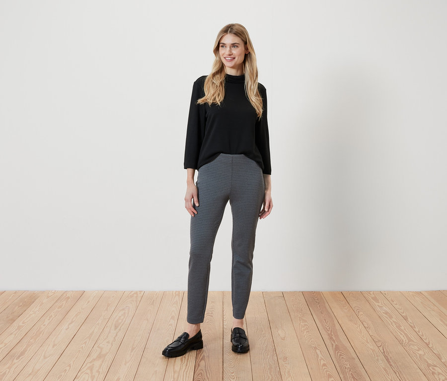 Femme blonde portant un haut noir à manches trois-quarts et un pantalon gris à motifs.