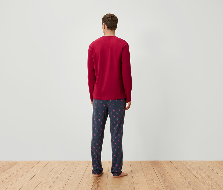 Un homme, vu de dos, porte un haut de pyjama rouge à manches longues et un pantalon de pyjama bleu marine avec un motif de rennes.