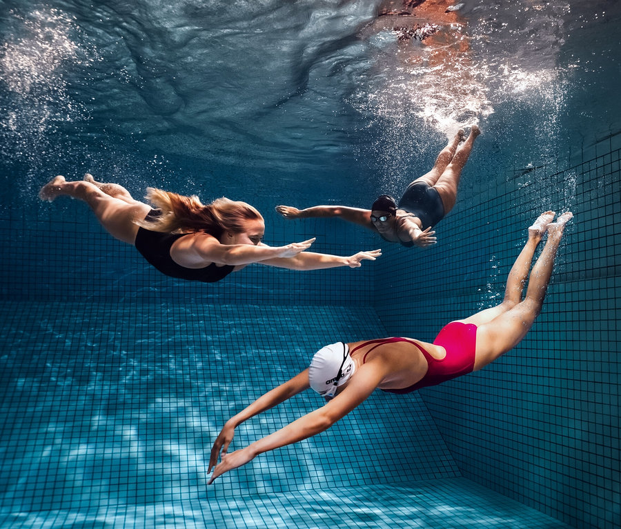 Trois femmes nagent sous l'eau dans une piscine. L'une d'elles porte un maillot de bain sculptant Lara C-Cup arena.
