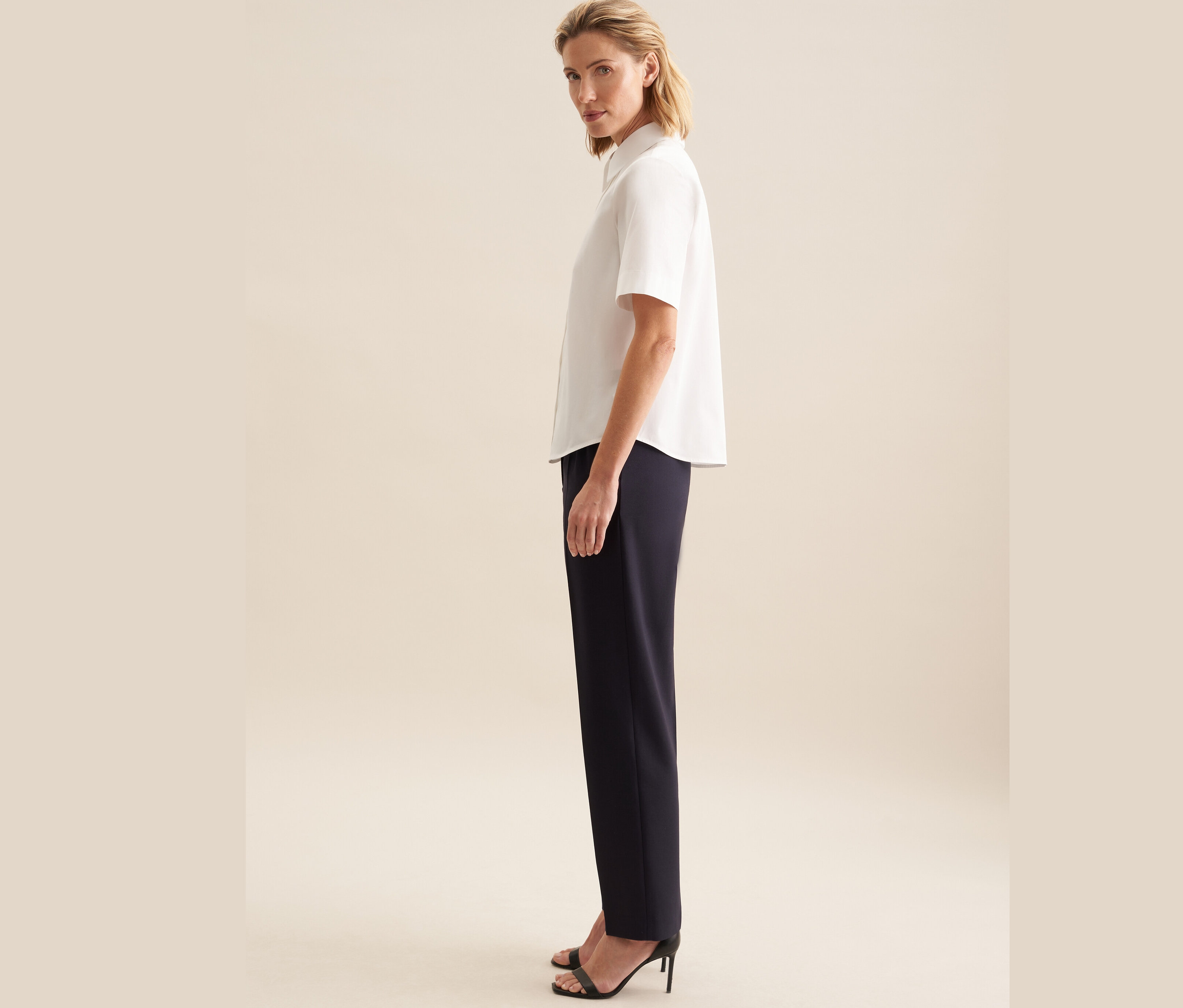 Femme posant en chemisier à manches courtes Seidensticker blanc et pantalon bleu marine.