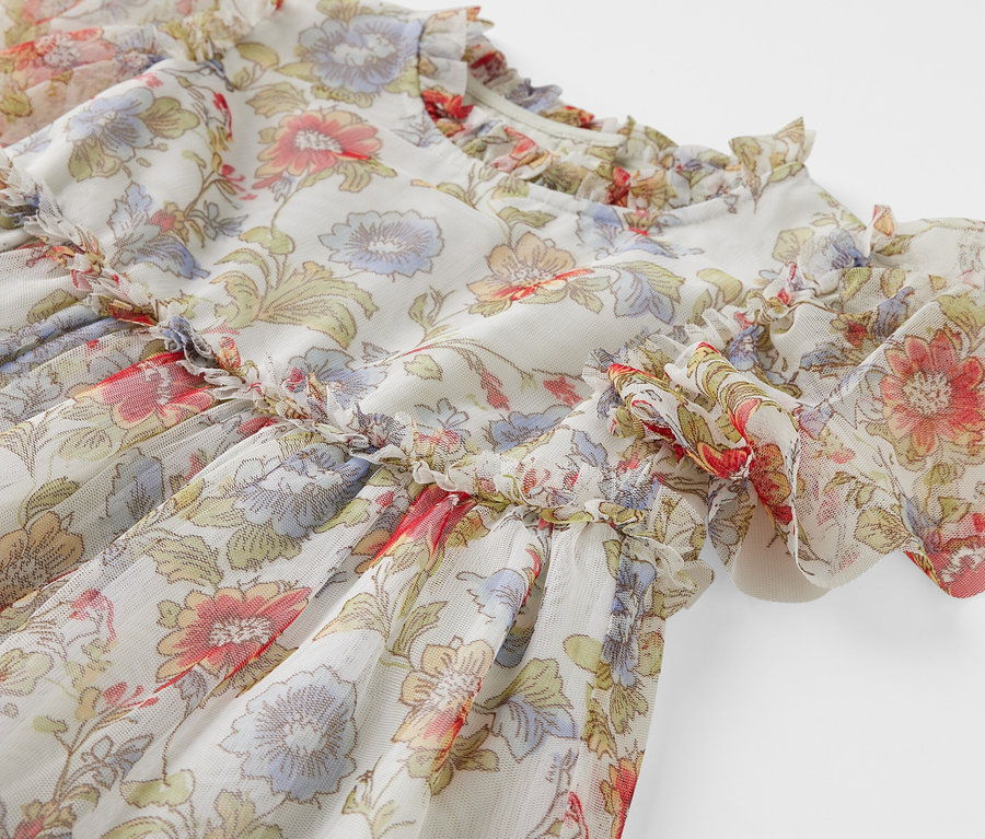 Gros plan sur une robe en tulle pour enfant avec un motif floral et des volants.