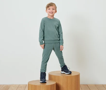 Un garçon en survêtement vert se tient sur un socle en bois.