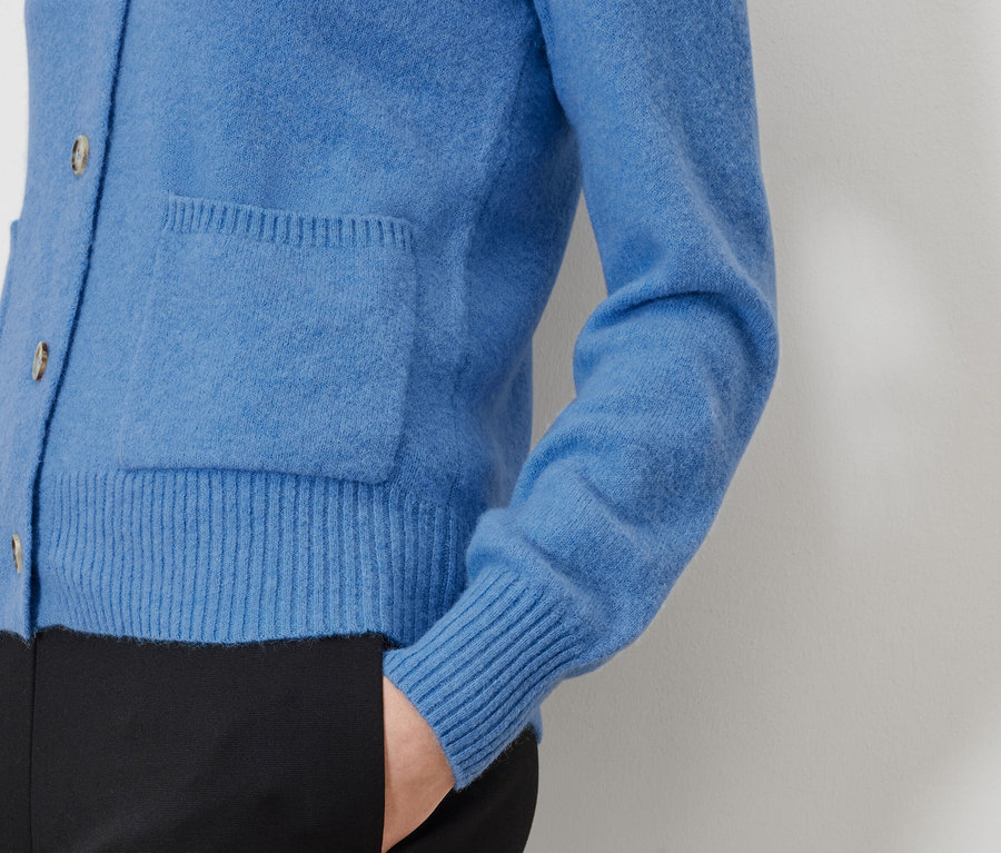 Détail d'un cardigan bleu avec poche et pantalon noir.