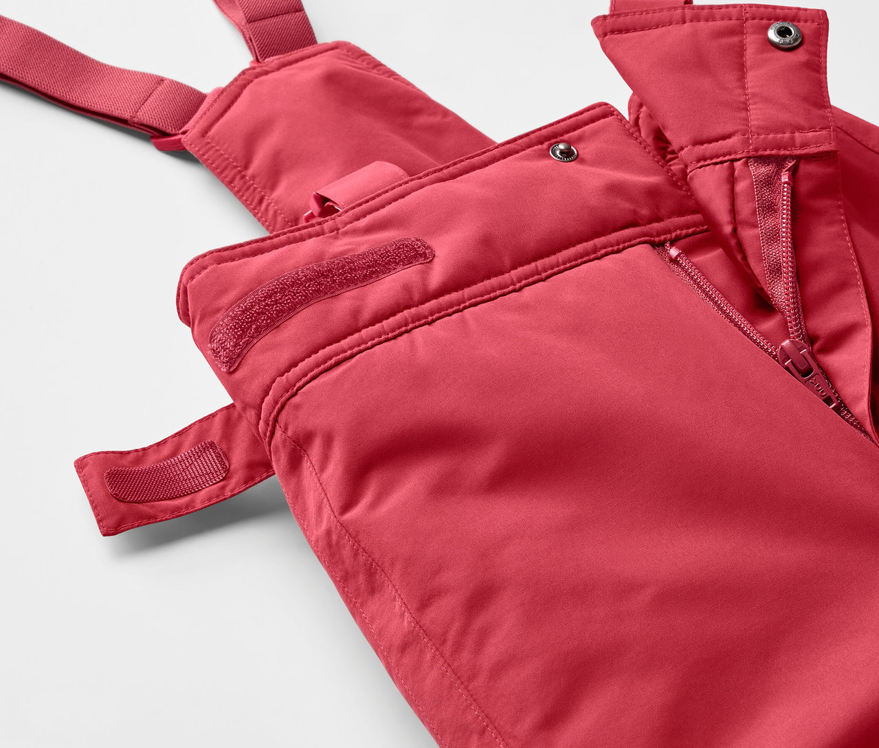Gros plan sur un pantalon de ski rouge à bretelles avec fermeture éclair.