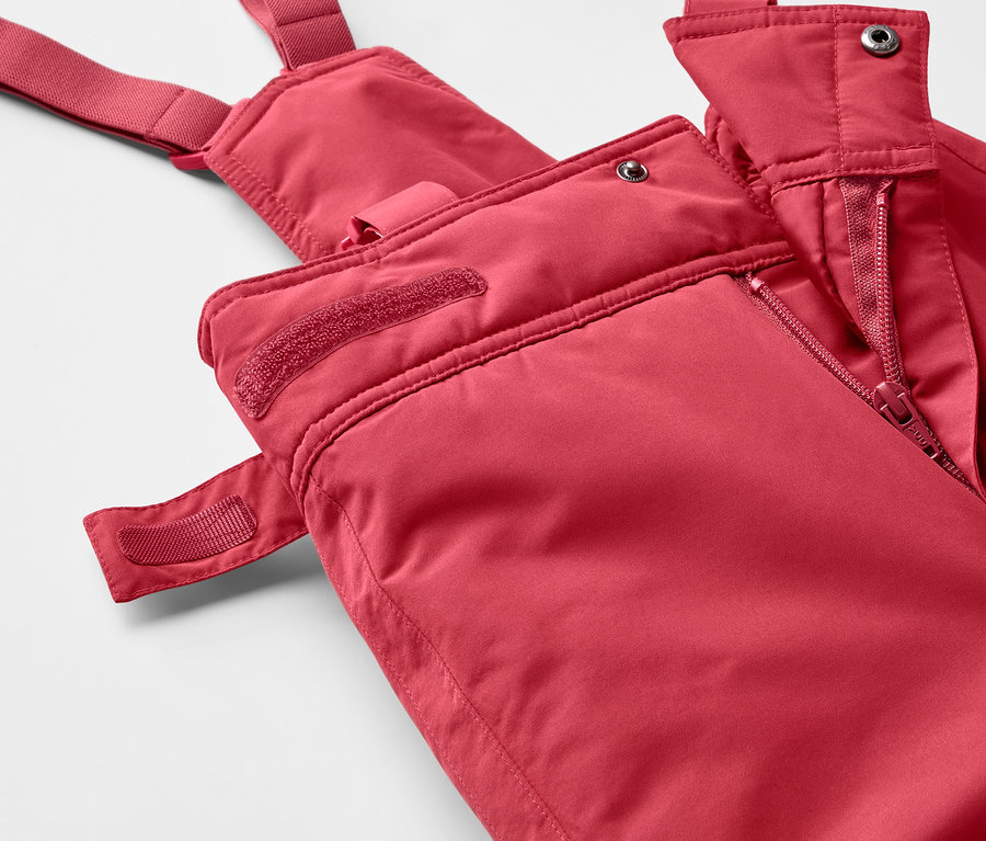 Gros plan sur un pantalon de ski rouge à bretelles avec fermeture éclair.